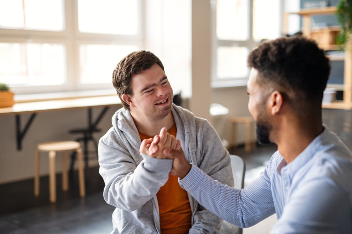 Two friends smiling and holding hands together in a supportive gesture.