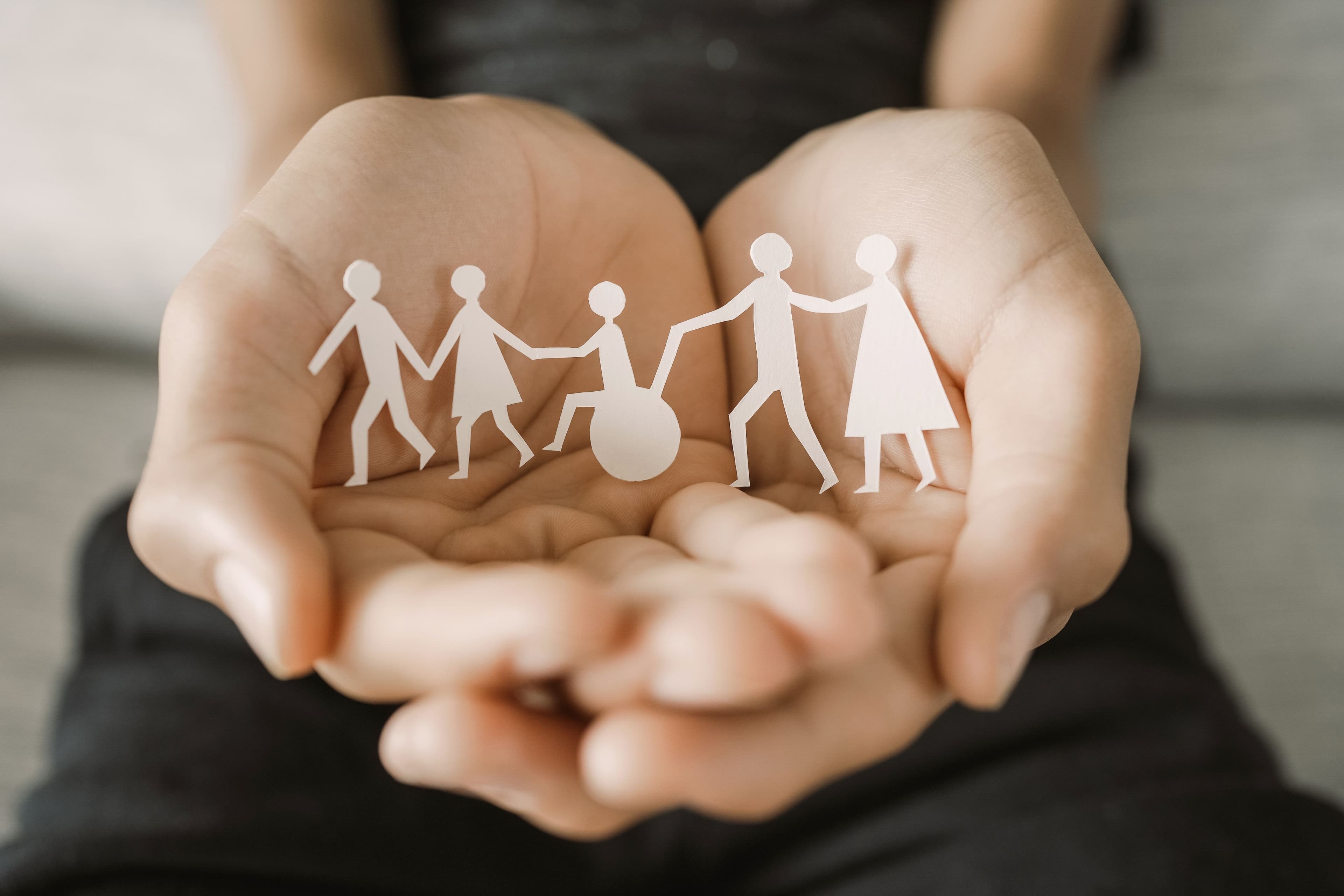 A person holds a paper chain of five figures, including one in a wheelchair, all joined hand in hand.